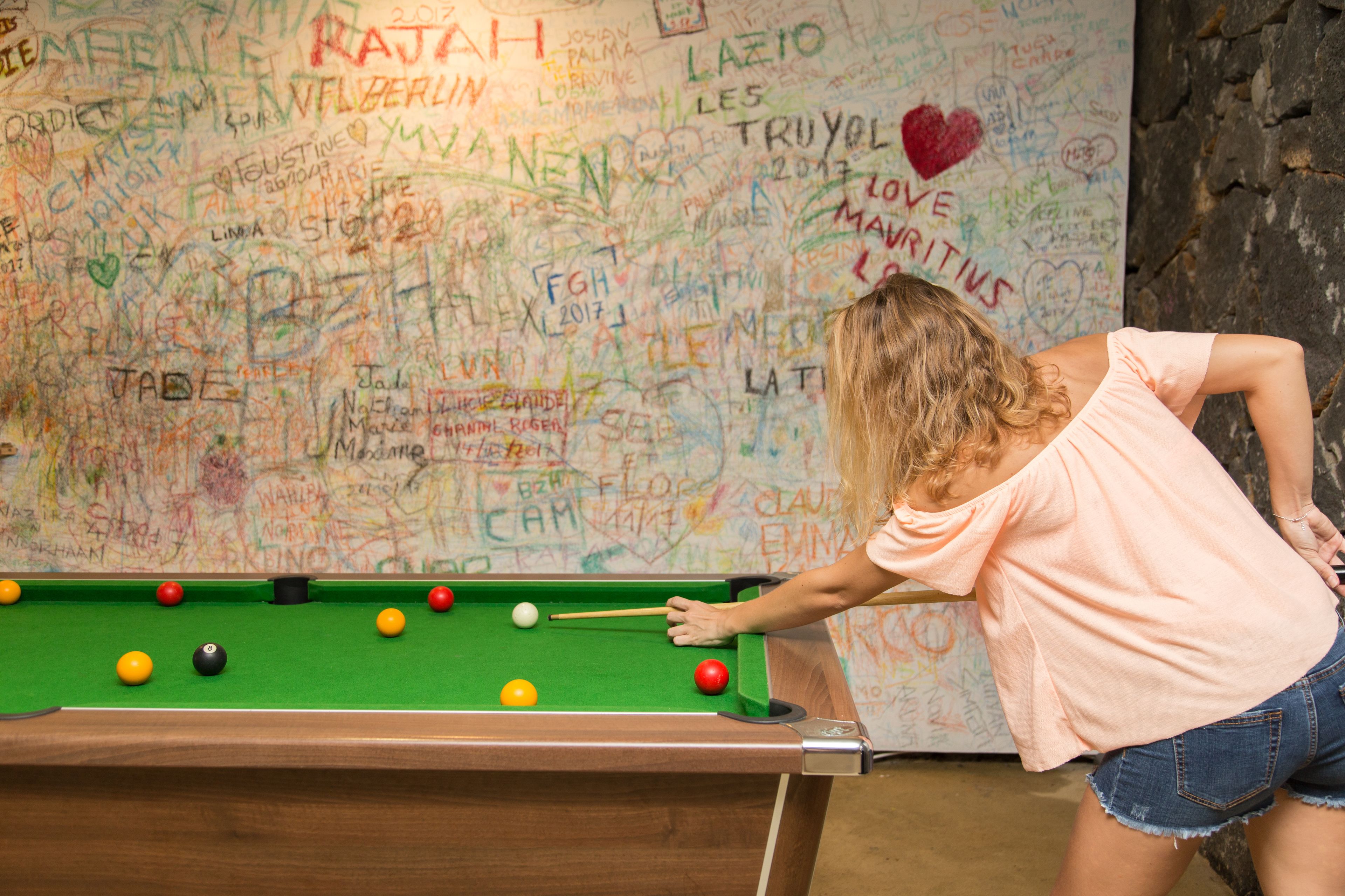 A person playing pool in front of a wall covered with various writings and drawings.