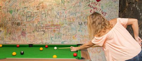 A person playing pool in front of a wall covered with various writings and drawings.