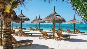 A beach with wooden lounge chairs and thatched umbrellas, a palm tree, and a clear blue sea. - Friday Attitude (Trou d'Eau Douce)