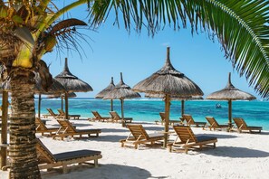 Una playa con sillones de madera y sombrillas de paja, una palmera y un mar azul y transparente.