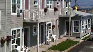 A two-story building with a balcony, white railings, and a small porch area with white plastic chairs. - Hotel Motel Panorama de Perce (Perce)