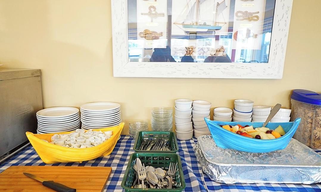 A buffet setup with stacked plates, bowls of food, and utensils on a checkered tablecloth.