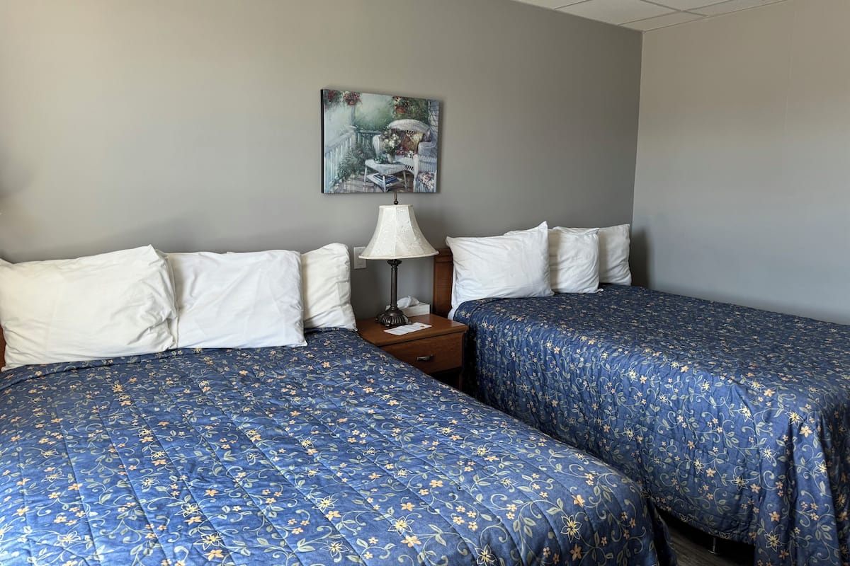 A hotel room with two beds, each with a blue floral bedspread, white pillows, and a nightstand with a lamp.