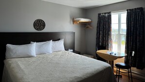 A hotel room with a large bed, a bedside table, a small desk, and a window with curtains. - Hotel Motel Panorama de Perce (Perce)