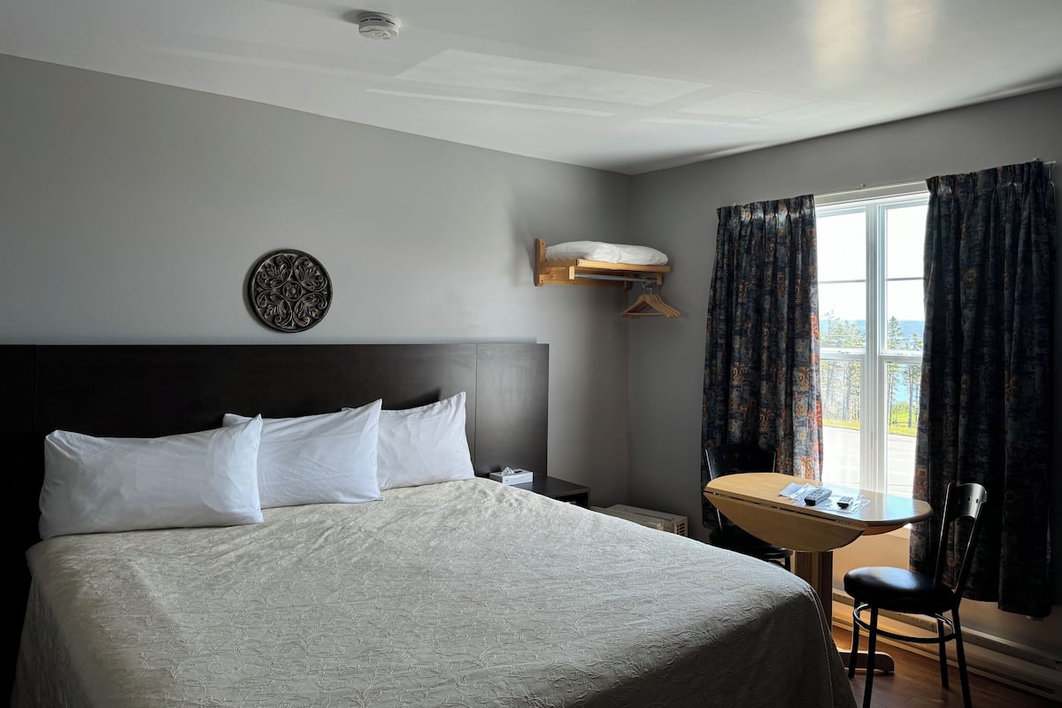A hotel room with a large bed, a bedside table, a small desk, and a window with curtains.