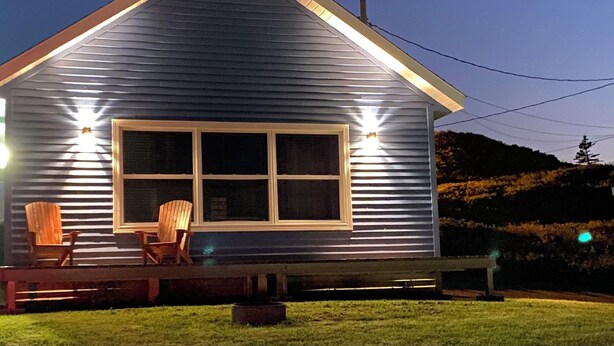 A house with a large window, a porch with two chairs, and a small fire pit. - Hotel Motel Panorama de Perce (Perce)