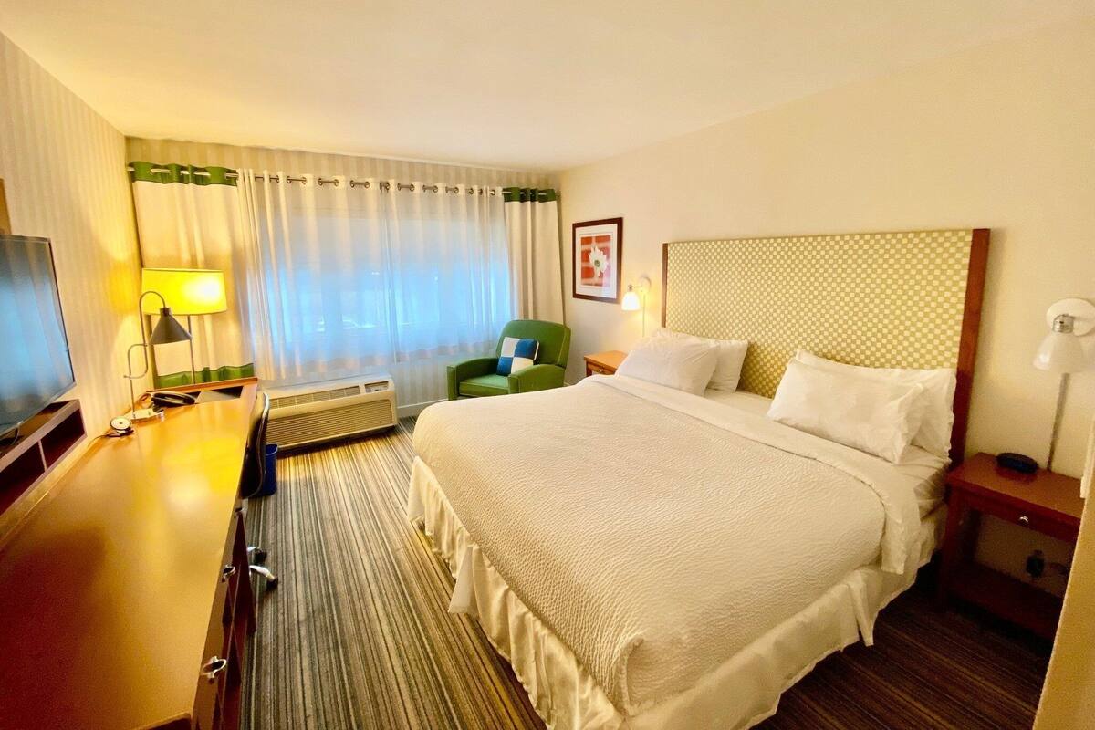 Een hotelkamer met een groot bed, een bureau met lamp, een stoel en een televisie.