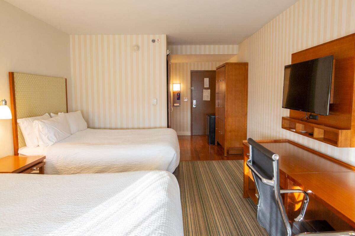 Hotelkamer met twee bedden, een bureau, een televisie en een badkamer zichtbaar door een geopende deur.