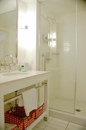 Un baño con lavamanos blanco, espejo y ducha con mampara de vidrio.