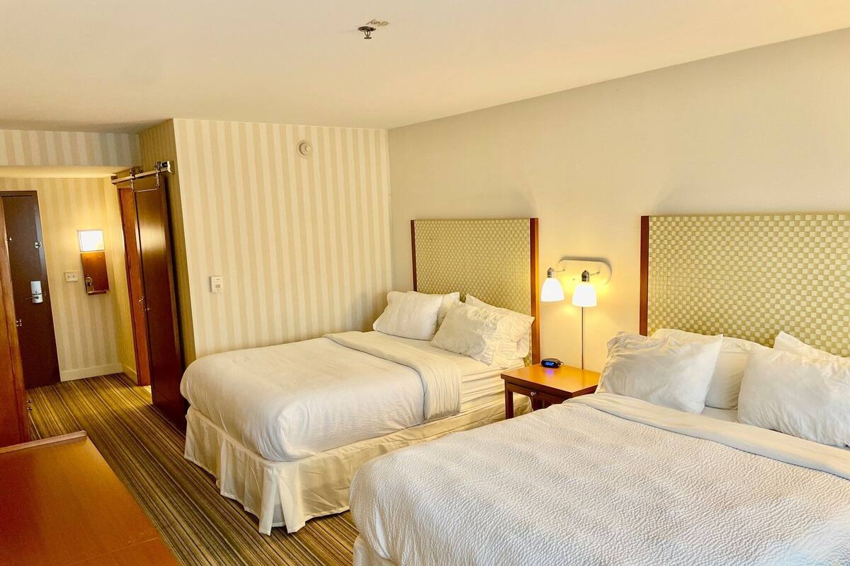 Een hotelkamer met twee bedden, een houten vloer, gestreept behang en een nachtkastje met een lamp.