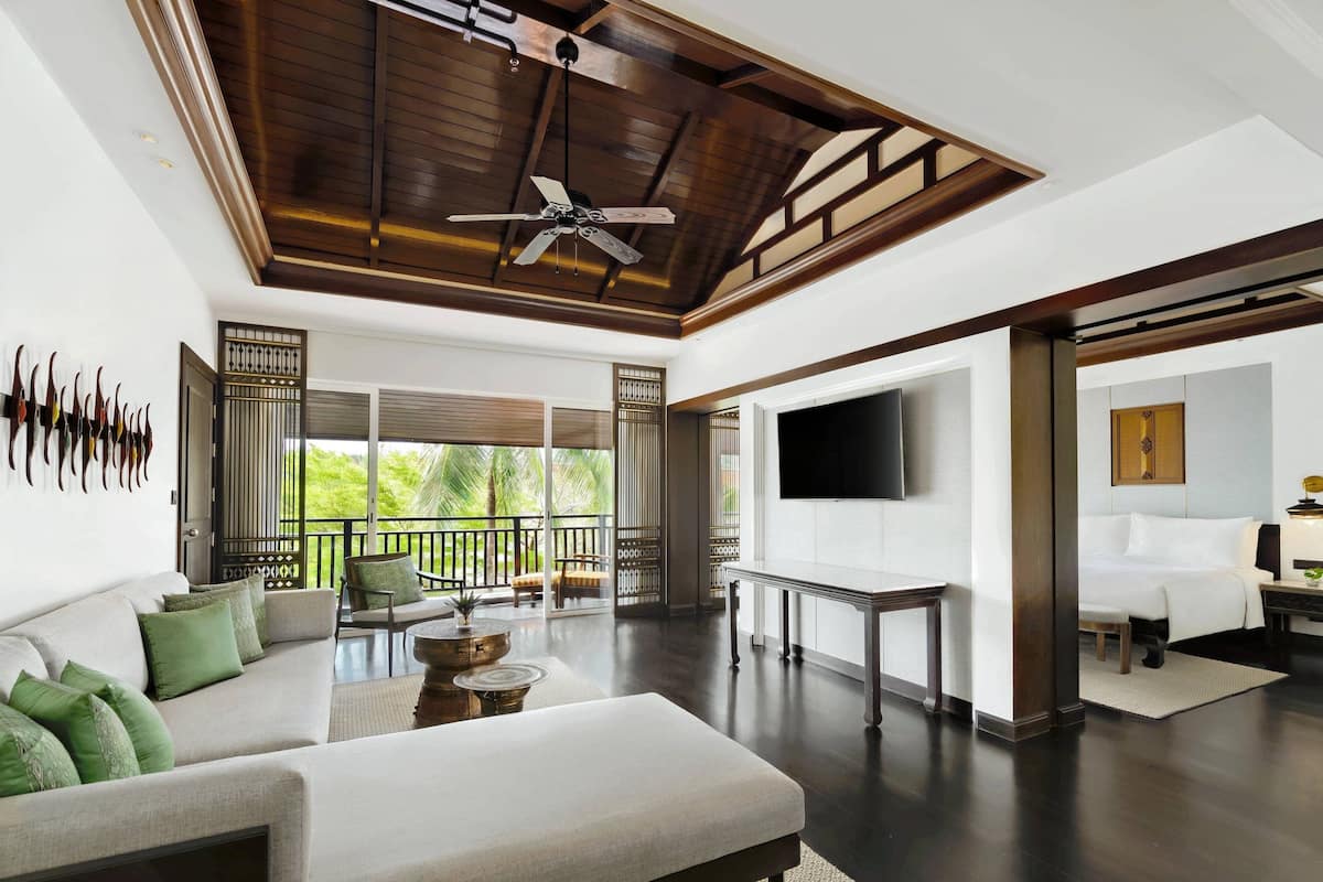A spacious living area with a ceiling fan, a sofa with green cushions, a TV mounted on the wall, and a balcony with a view of greenery.