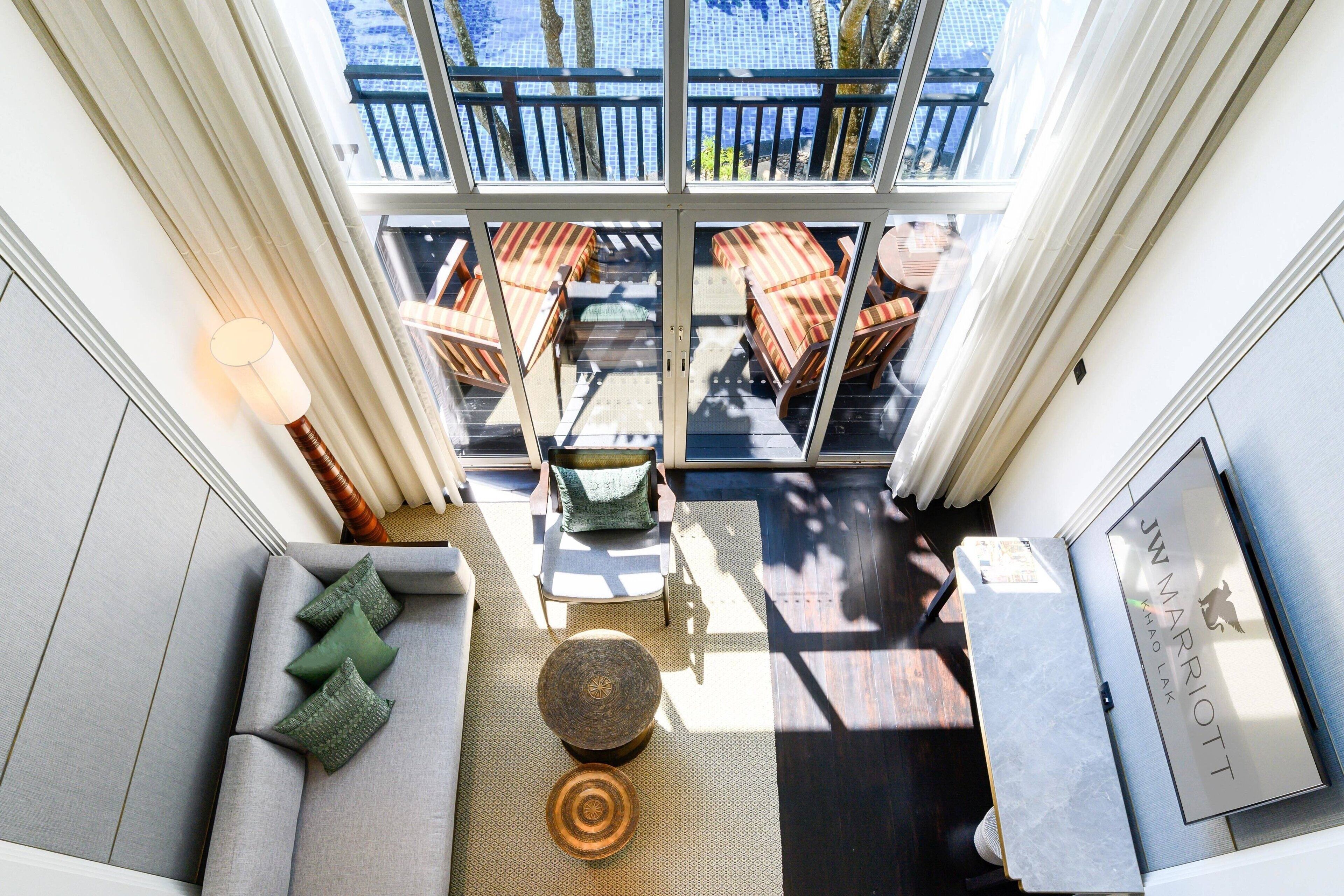 A modern hotel room with a large sliding glass door leading to an outdoor seating area with wicker furniture.