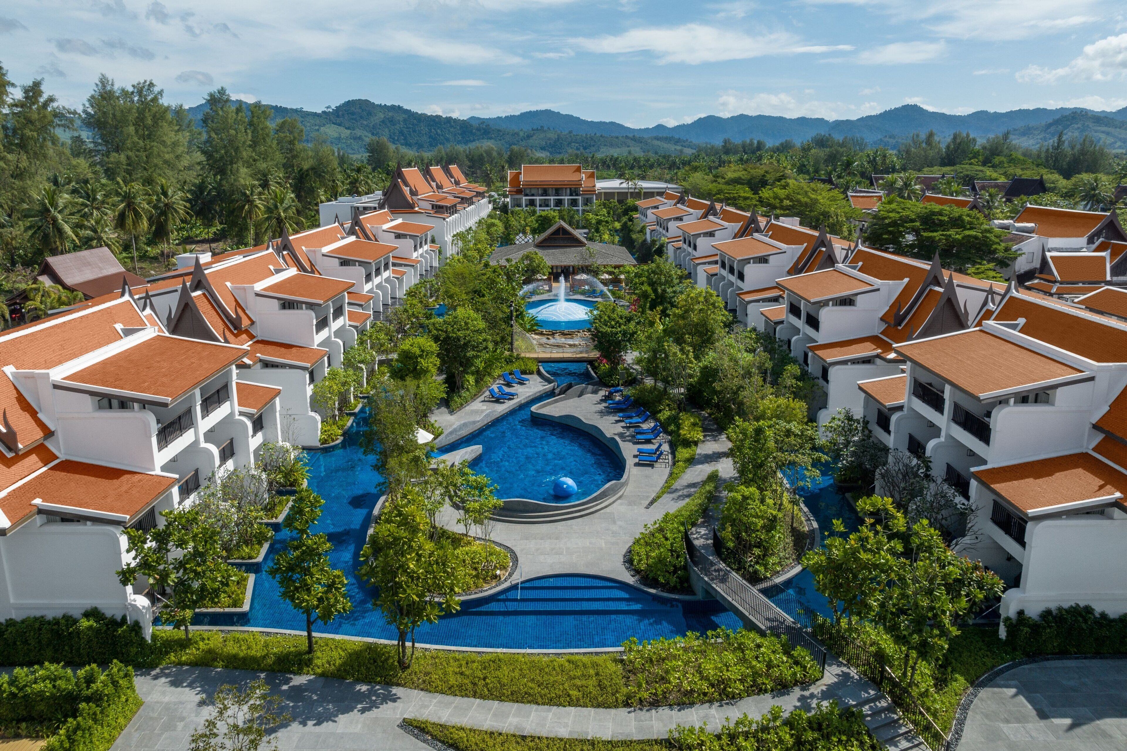 A resort with multiple buildings, a central swimming pool, and surrounding greenery.