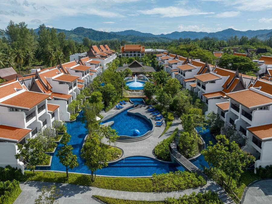 A resort with multiple buildings, a central swimming pool, and surrounding greenery.