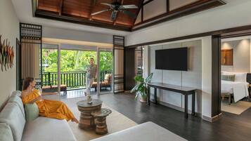 Una sala de estar moderna con un sofá, una mesa de centro, un televisor montado en la pared y un balcón con vistas a la vegetación.