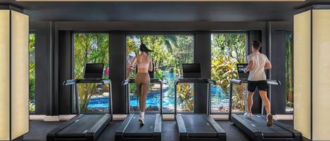 A gym with treadmills aligned in front of large windows with a view of a pool and greenery.