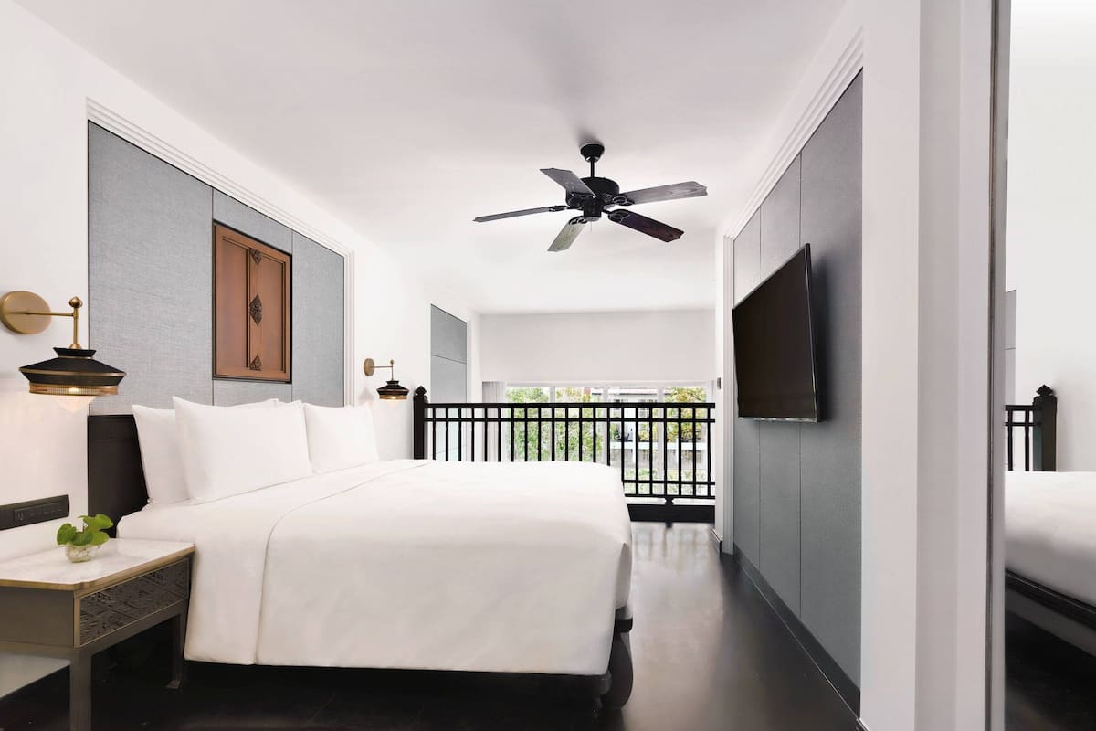 Ein modernes Hotelzimmer mit einem großen Bett, einem Deckenventilator, einem an der Wand montierten Fernseher und einem Balkon mit Blick.