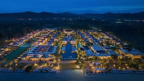 Luchtbeeld van een resort met meerdere gebouwen, een centraal gelegen zwembad en omliggende palmbomen.