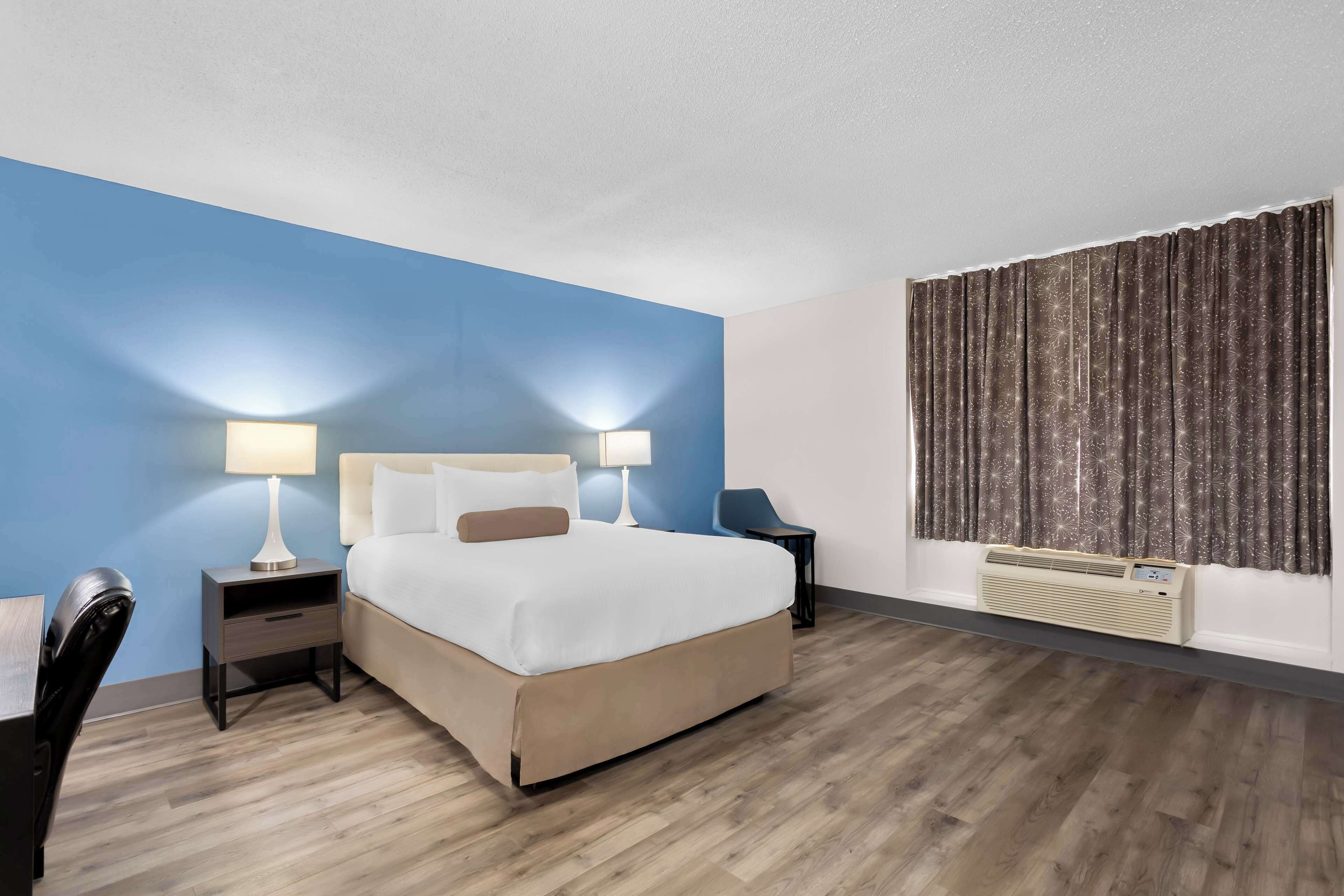 A hotel room with a large bed, two bedside tables with lamps, a chair, a desk, and a window with curtains.