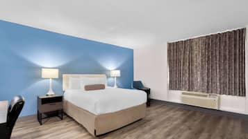 A hotel room with a large bed, two bedside tables with lamps, a chair, a desk, and a window with curtains.