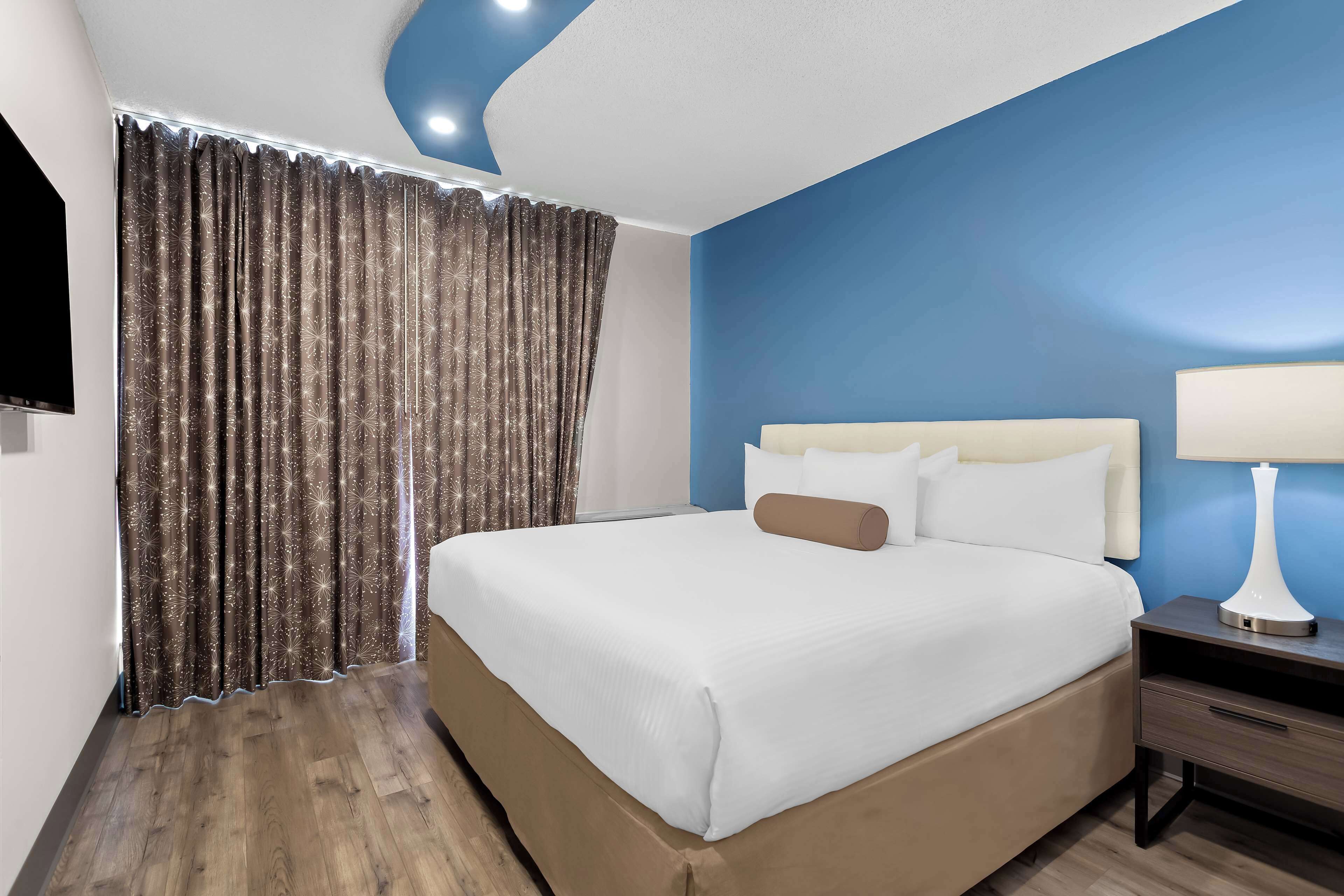 A hotel room with a large bed, a nightstand with a lamp, and a TV on the wall.