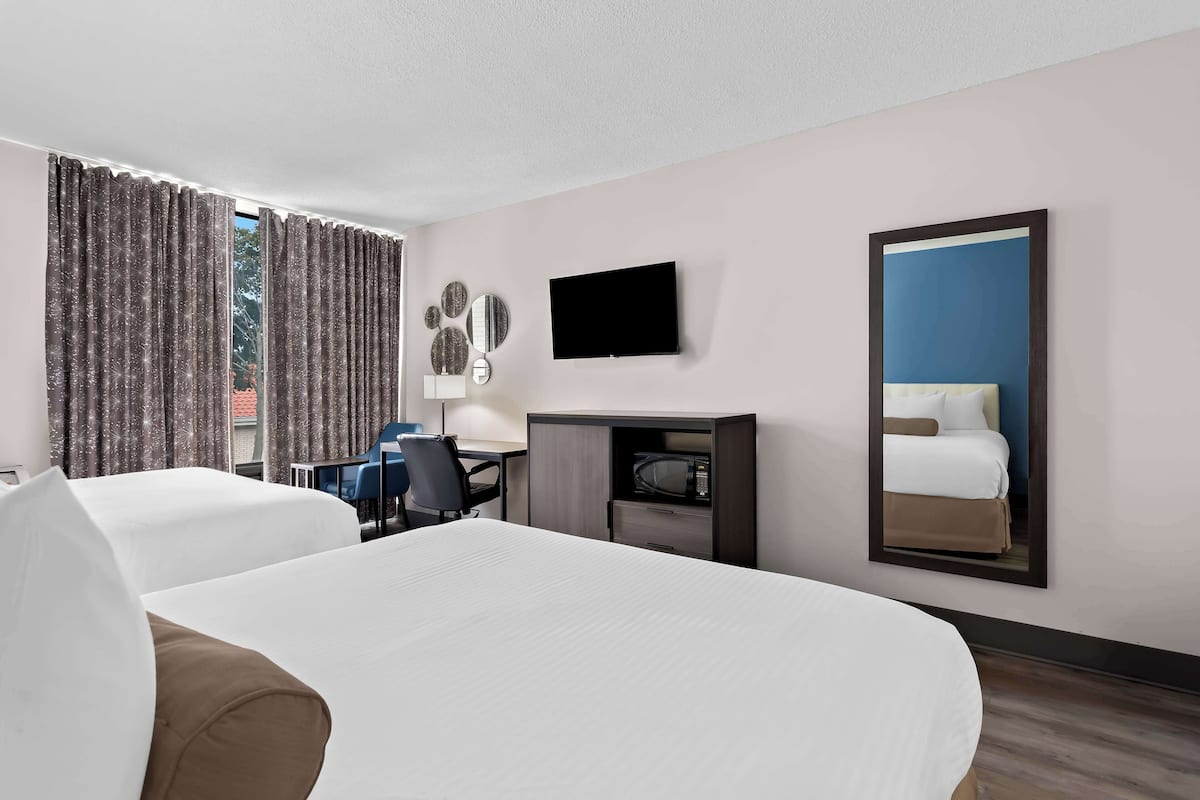 A hotel room with two beds, a desk, a chair, a TV, and a mirror.