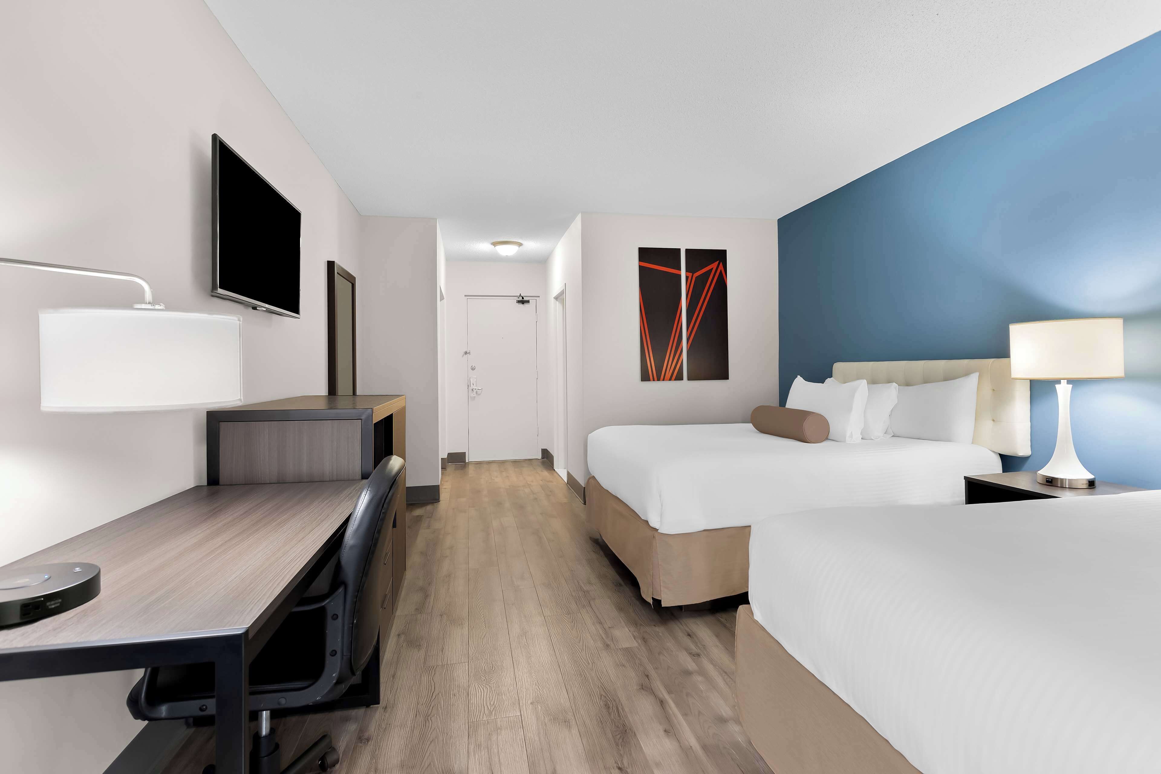 Habitació d'hotel amb escriptori, dos llits, televisió i un quadre a la paret.
