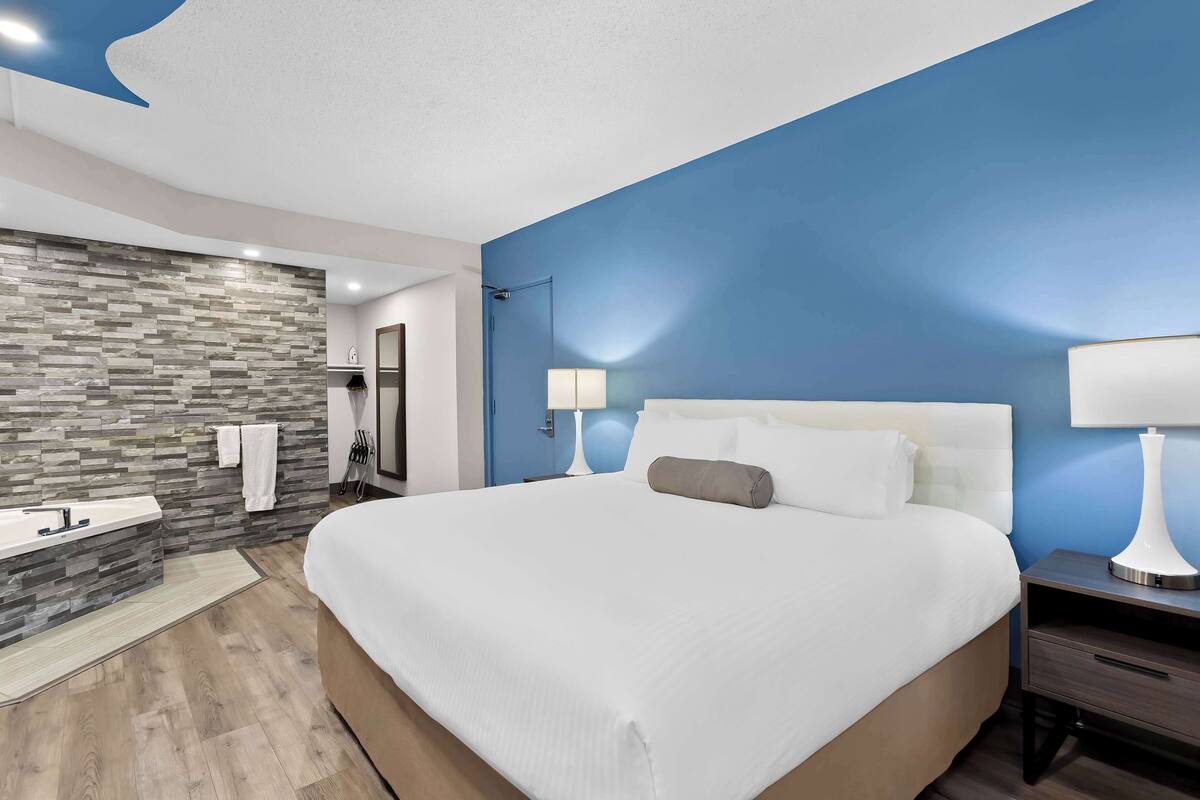 A modern hotel room with a large bed, a built-in bathtub, and a stone wall.