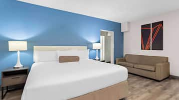 A hotel room with a large bed, two bedside tables with lamps, a beige sofa, and a blue accent wall.