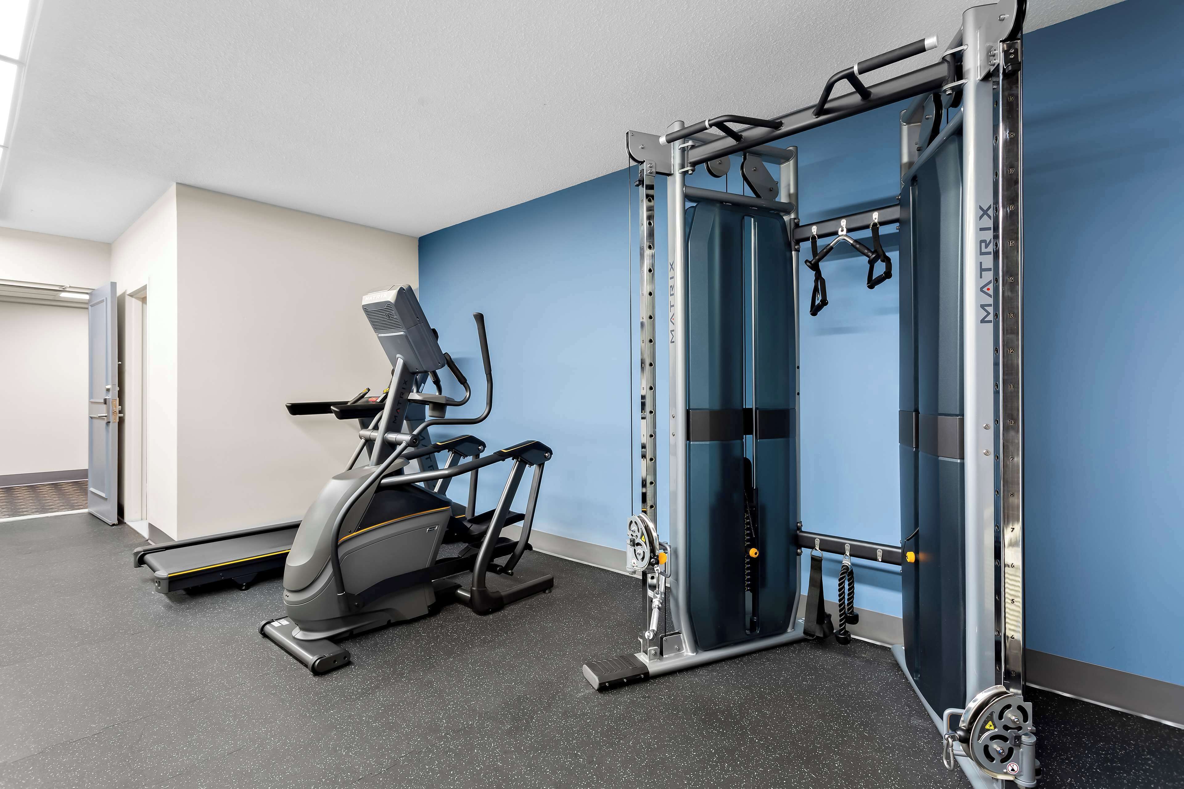 Un gimnasio con cinta de correr, máquina de pesas y barra para dominadas.