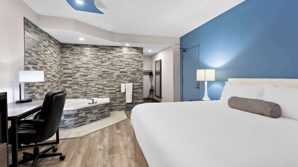 A modern hotel room with a large bed, a desk with a chair, a bathroom with a stone backsplash, and a blue accent wall. - SureStay Plus by Best Western Windsor (Windsor)