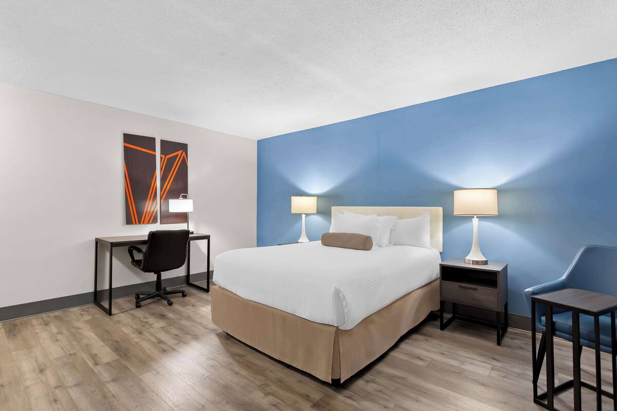 A hotel room with a bed, desk, chair, and nightstands with lamps.