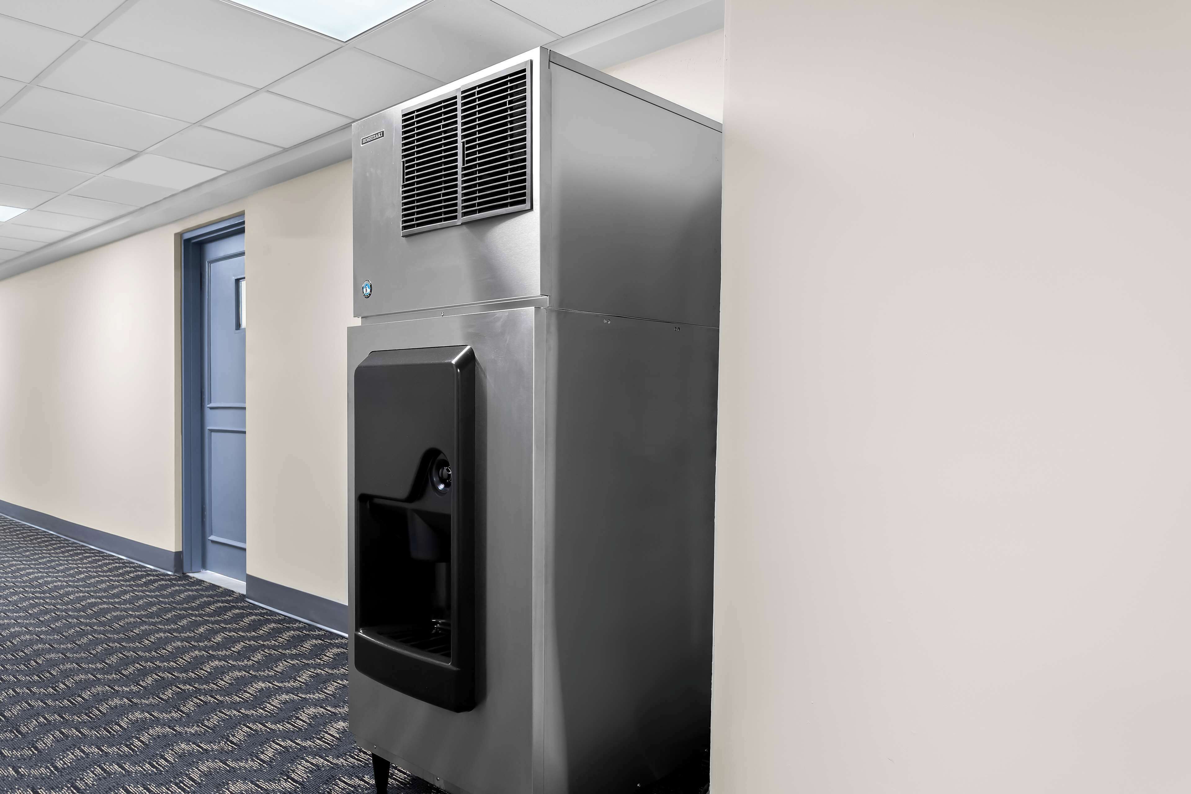 Un mini-bar en acier inoxydable, doté d’un distributeur de boissons, situé dans un couloir d’hôtel.