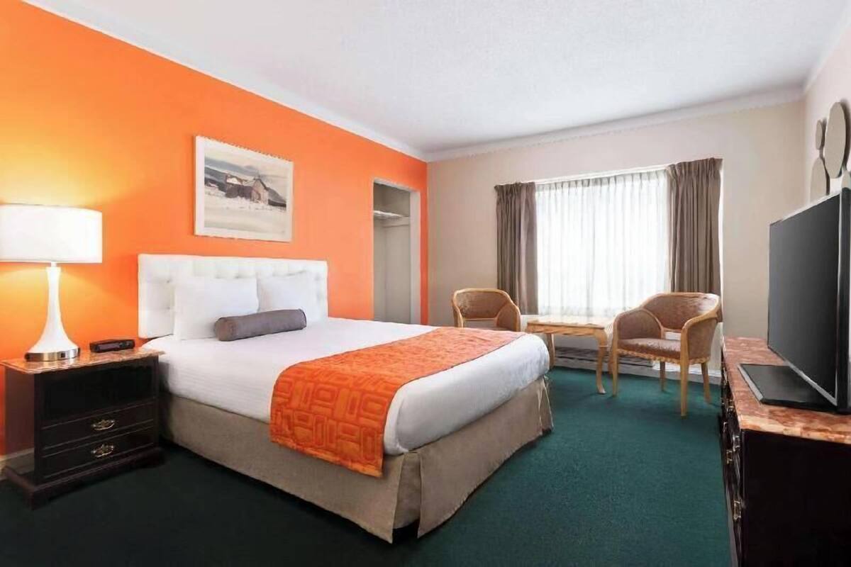 A hotel room with a bed, a desk, a chair, a TV, and a nightstand.