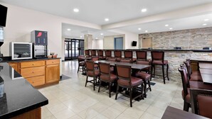 A spacious dining area with multiple tables and chairs, a kitchen area with appliances, and a stone accent wall. - SureStay Plus by Best Western Windsor (Windsor)