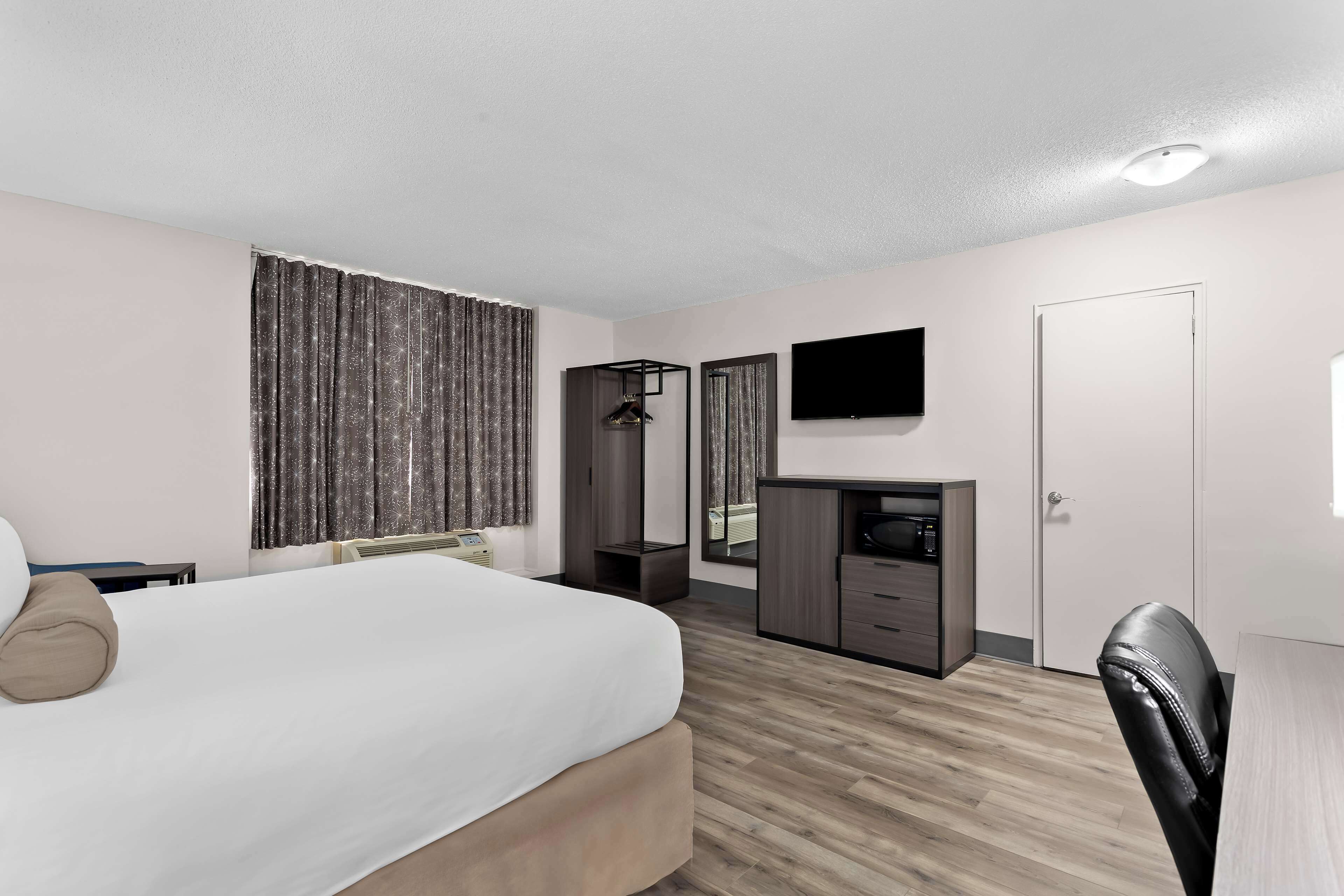 A hotel room with a bed, a desk, a chair, a television, and a wardrobe.
