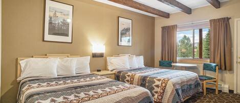 Una habitación de hotel con dos camas, una mesita, una silla y un ventanal con cortinas.