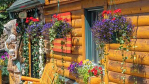 A wooden cabin with flower baskets hanging from the exterior, a wooden sculpture, and a sign with the word "PIZZA". - Spirit Lake Lodge (Grand Lake)