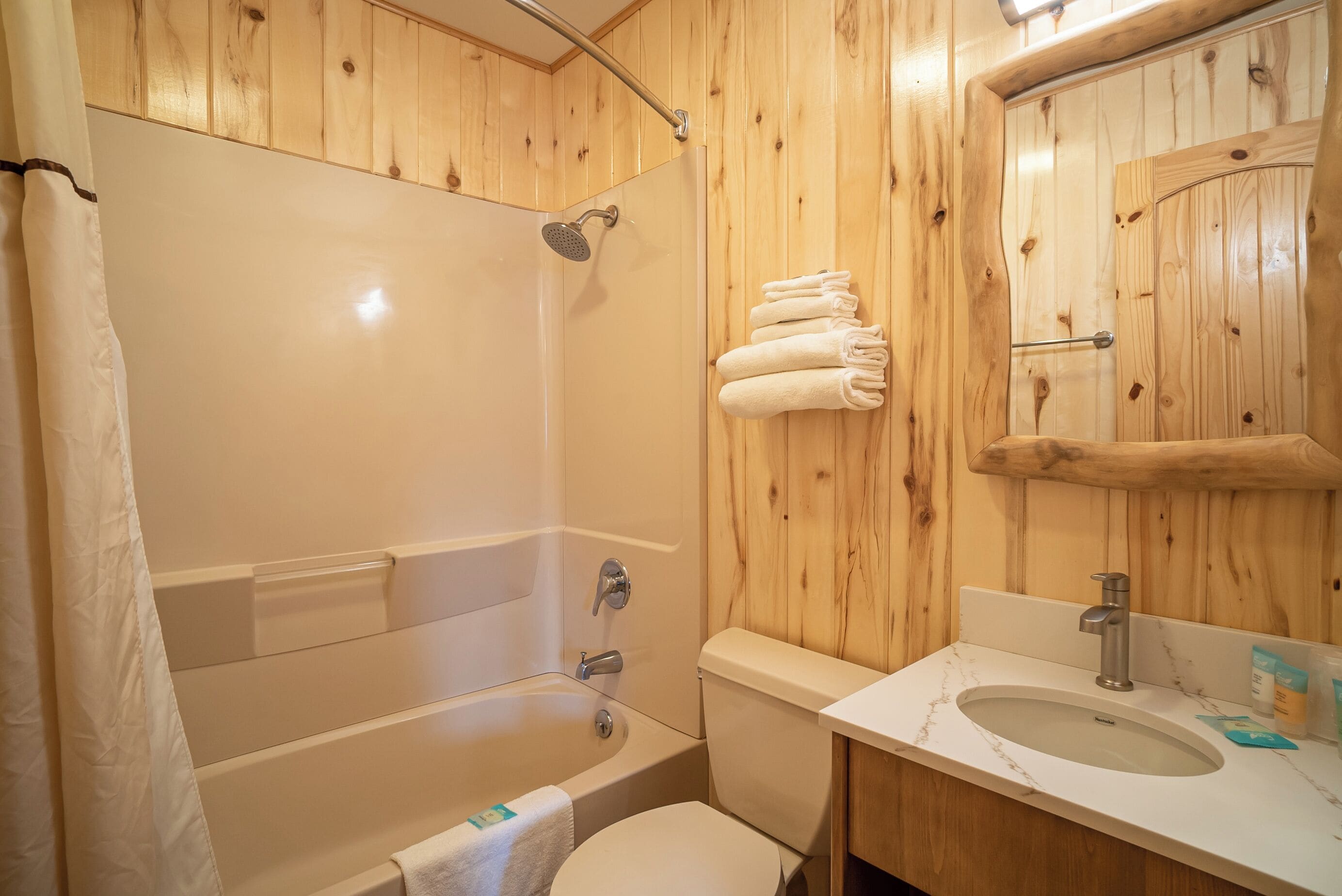 Een badkamer met houten lambrisering, een bad, toilet en een wastafel met spiegel.