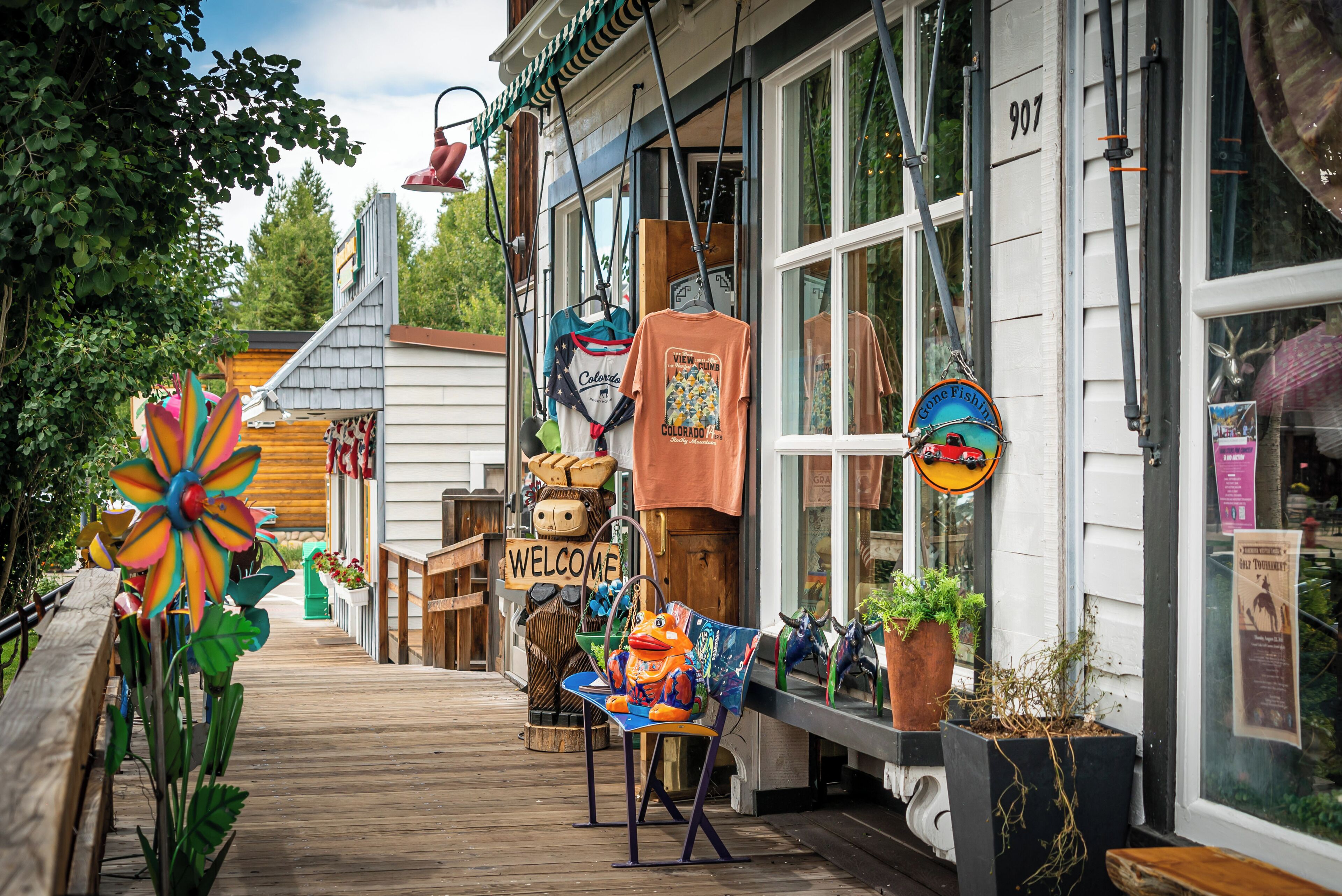 Une terrasse en bois avec une pancarte d’accueil, un moulinet coloré et divers objets exposés à l’extérieur d’un bâtiment.