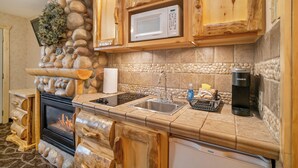 A kitchen with a stone wall, wooden cabinets, a microwave, a sink, and a coffee maker. - Spirit Lake Lodge (Grand Lake)