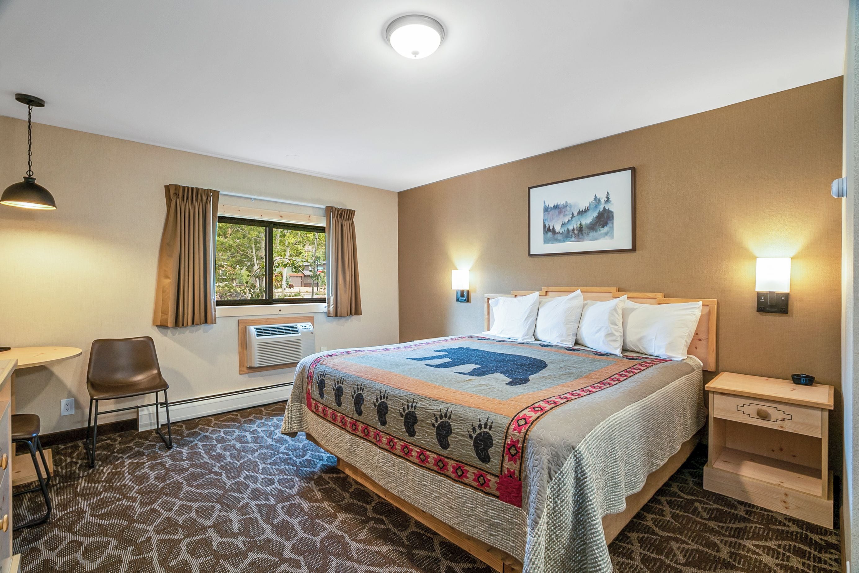 A hotel room with a bed, a desk, a chair, a window with curtains, a wall-mounted picture, and a patterned carpet.