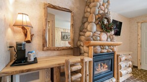 A cozy room with a stone fireplace, a wooden coffee table with a Keurig coffee maker, a microwave, and a mirror on the wall. - Spirit Lake Lodge (Grand Lake)