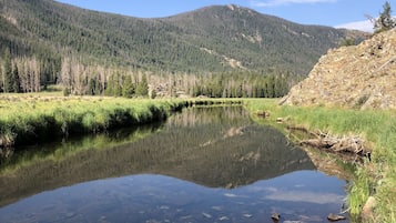 Visão nítida de uma paisagem montanhosa com um lago tranquilo refletindo as árvores e o céu ao redor.