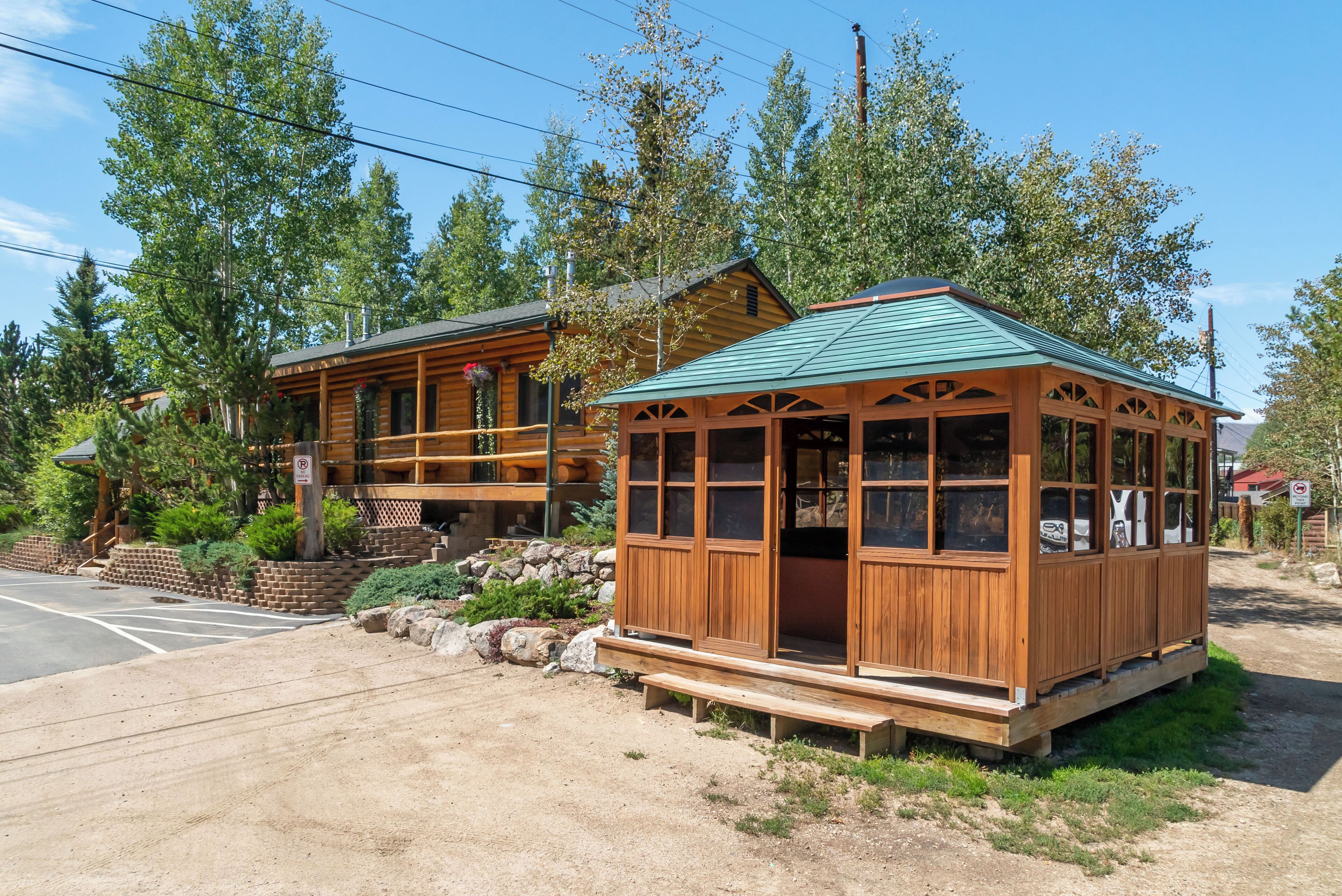Eine Holzhütte mit grüner Dachdeckung, einer Veranda und einem kleinen angebauten Anbau mit großen Fenstern.