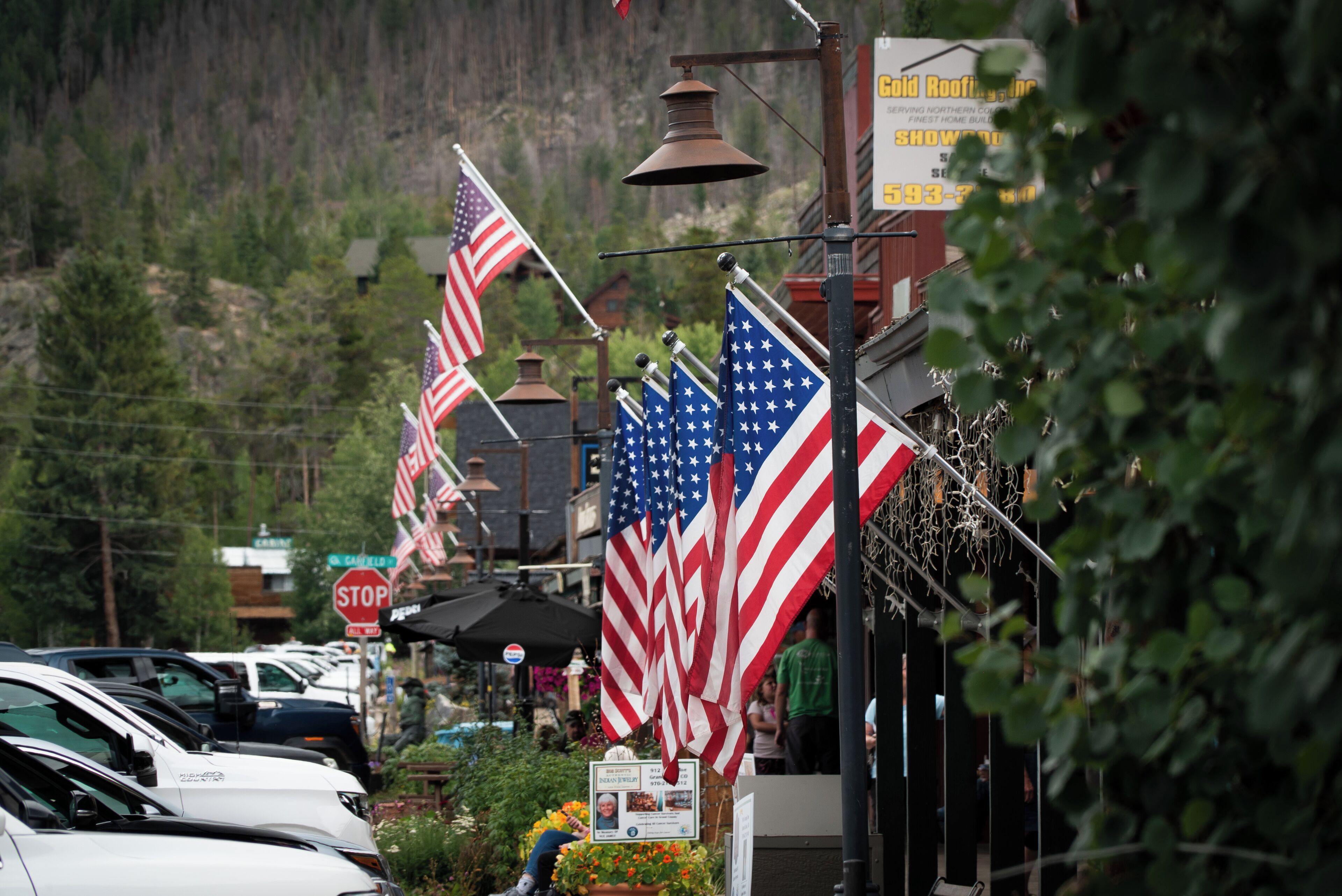A street lined with American flags, parked cars, and a stop sign.