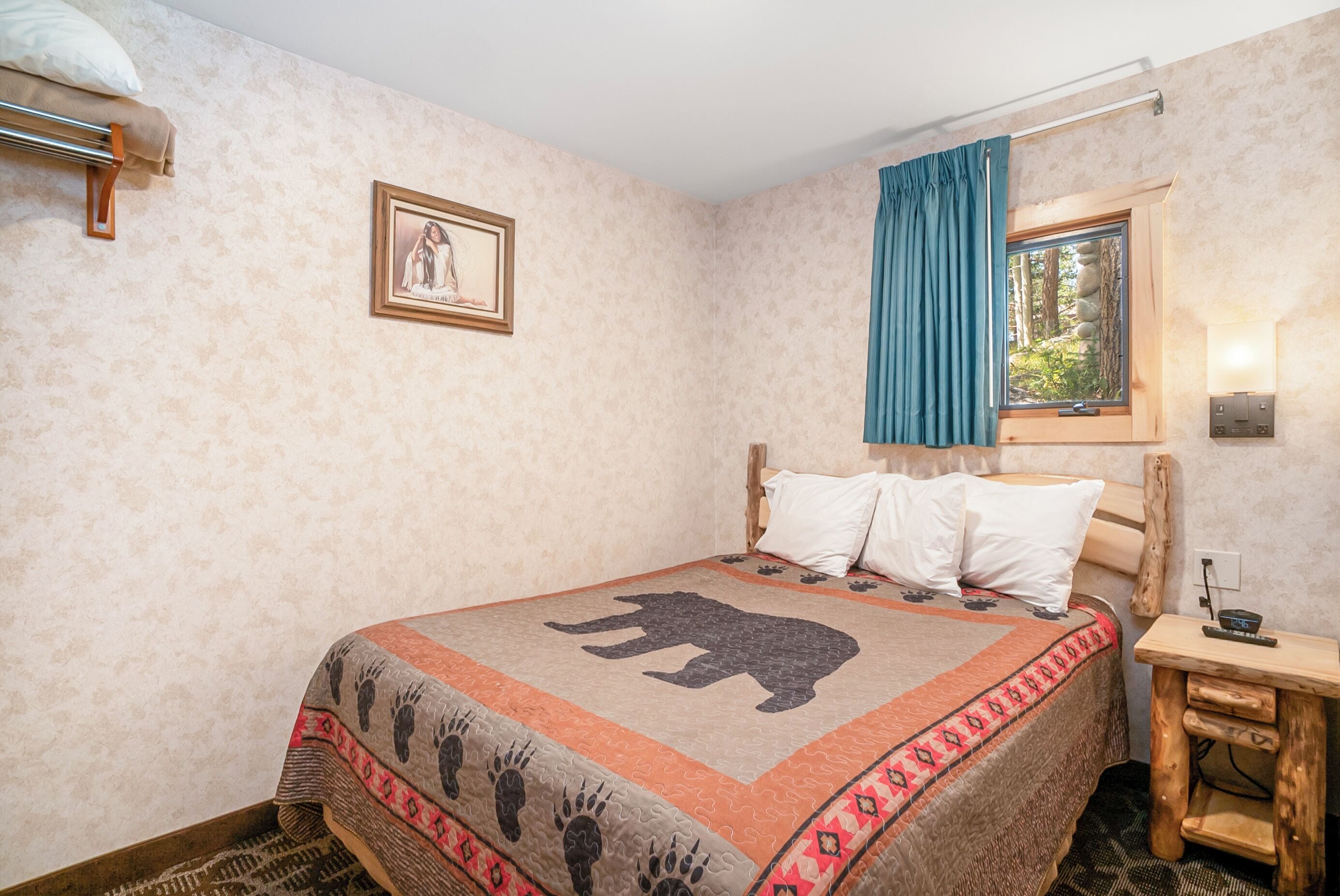 A bedroom with a bed featuring a bear design, a wooden nightstand, a framed picture on the wall, and a window with a curtain.