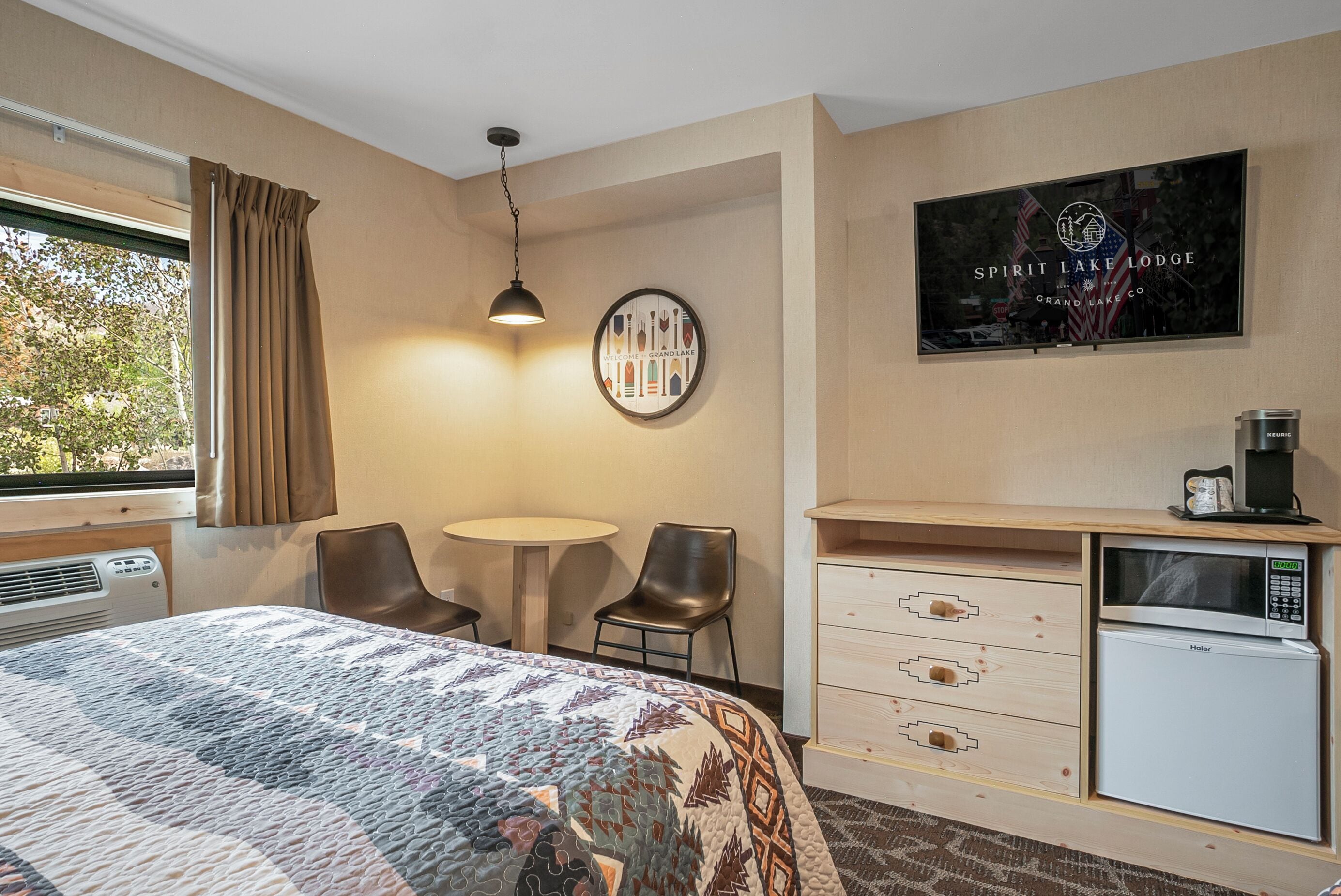 A hotel room with a bed, a desk with a computer, a refrigerator, and a window with curtains.