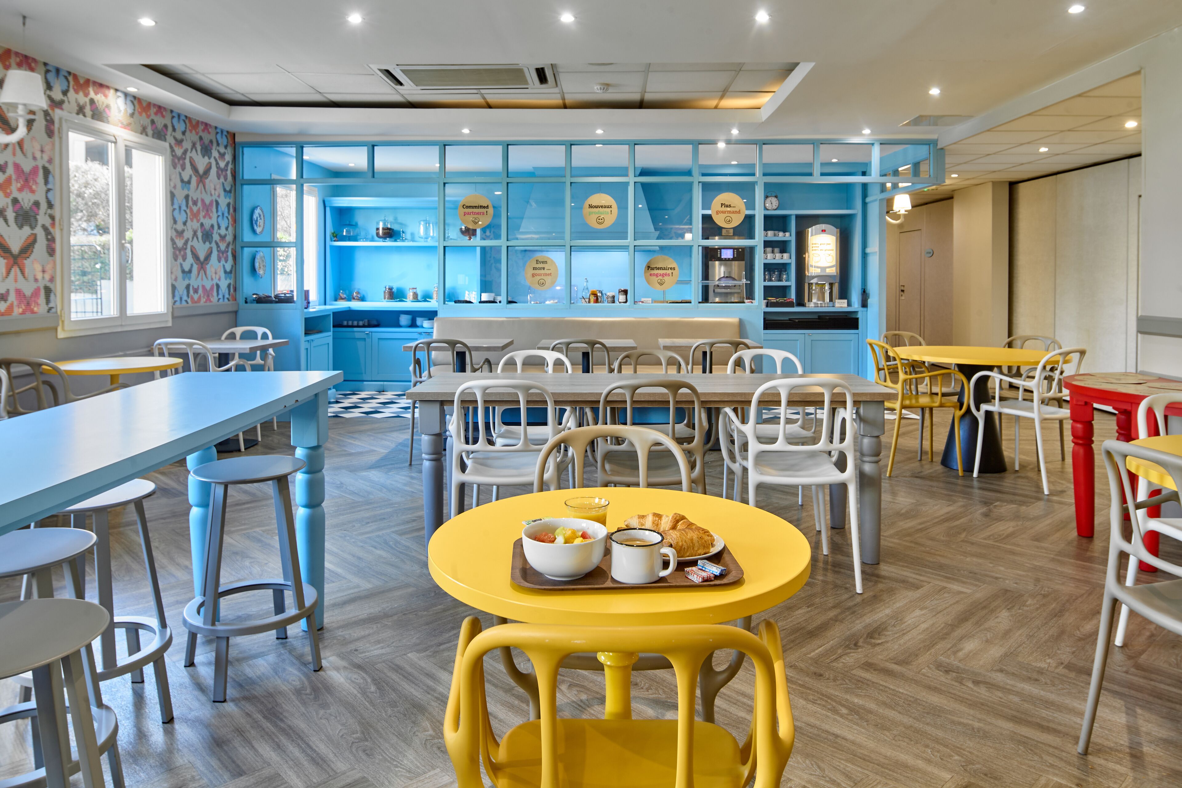 A restaurant with blue walls, white chairs, and a yellow table with breakfast.