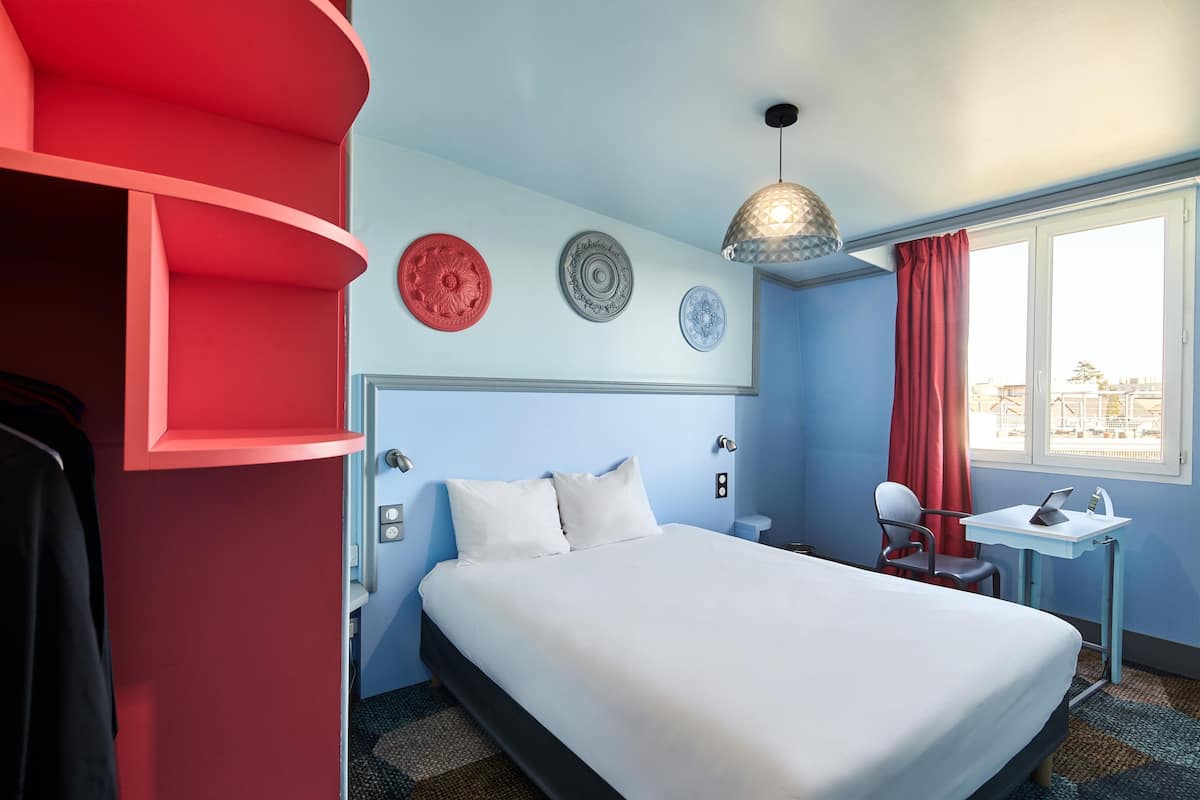 A hotel room with a bed, a desk, a chair, a lamp, and decorative plates on the wall.